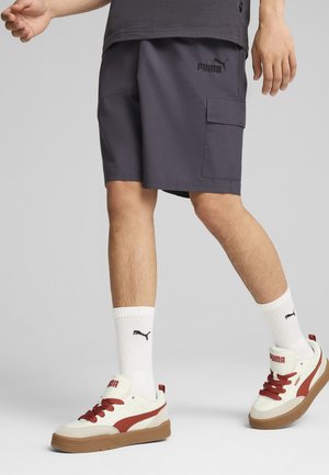 Harmaat cargo-shorts sivutaskulla, jotka on yhdistetty valkoisiin sukkiin ja kermaisiin urheilukengiin, joissa on punaisia yksityiskohtia. Kengissä on ruskeat kumipohjat.