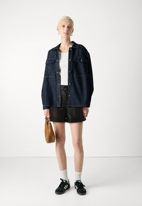 Tmavomodrá oversized džínová bunda, biele priliehavé tričko, čierne šortky, čierne tenisky s modrými akcentmi, biele ponožky a hnedá kabelka.