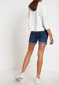 Vit stickad tröja i kombination med mörkblå denimshorts med uppvikt mudd och en klassisk passform, komplementerat av vita sneakers.