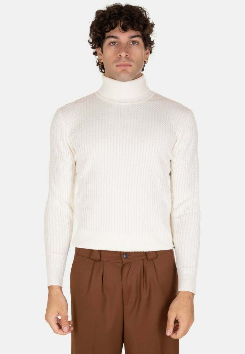 Maglione a collo alto bianco a coste con maniche lunghe, abbinato a un corpo aderente. Indossato con pantaloni marroni. Design semplice, tessuto testurizzato.