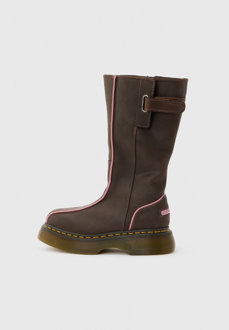 Botte en cuir marron mi-mollet avec des bordures roses, une semelle épaisse translucide, des coutures jaunes et une sangle latérale avec une boucle en métal.