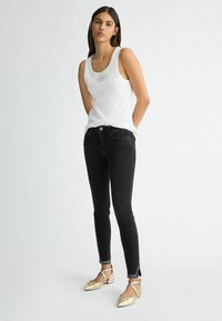 Top in cotone bianco a costine con scollo rotondo, abbinato a jeans skinny neri con orli borchiati e scarpe flat dorate con cinturini.