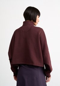 Suéter burdeos con cuello alto, corte holgado y hombros caídos. Tejido suave y texturizado con un diseño sencillo, apto para un uso casual.
