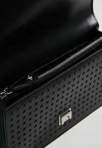 Borsa a tracolla nera in pelle con motivo a stelle in rilievo, accessori in argento e una tasca con zip nella parte superiore per una chiusura sicura.