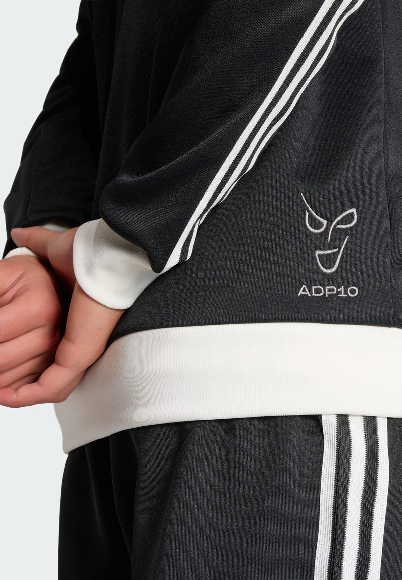 Haut de sport noir avec des accents blancs et trois bandes blanches le long des manches. Logo brodé "ADP10" sur le côté. Texture lisse.