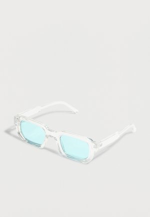 Klare rechteckige Brille mit dicken transparenten Fassungen und hellblauen getönten Gläsern, die auf einer weißen Oberfläche liegen.