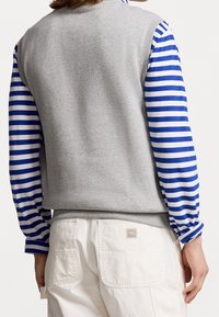 Šedá mikina s dlouhými rukávy modro-bíle pruhovanými, kombinovaná s bílými cargo kalhotami. Výrazné detaily zahrnují nášivku s logem na kalhotách.