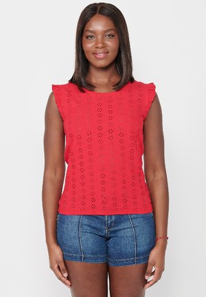 Rode mouwloze blouse met een eyelet patroon, gegolfde randen en een getailleerde pasvorm. Gecombineerd met jeanshorts. Heldere en gestructureerde uitstraling.
