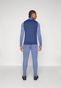 Sportstøj bestående af en navy ærmeløs top og en lyseblå langærmet trøje med blå detaljer, parret med matchende lyseblå leggings.