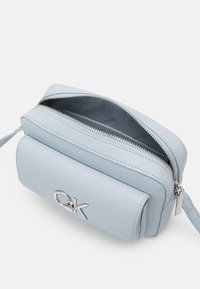 Lyseblå tekstureret læder crossbody taske med sølvlynlås, der har en frontlomme og et fremtrædende sølvlogo. Indersiden er grå.