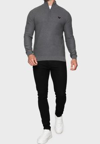 Pullover grigio a maglia con zip a un quarto, caratterizzato da un motivo testurizzato e logo ricamato. Abbinato a jeans neri e sneakers bianche.