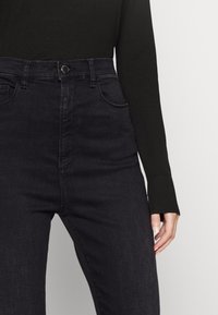High-waisted black jeans made of denim, featuring front pockets and a zip fly. The texture is smooth with minimal fading.