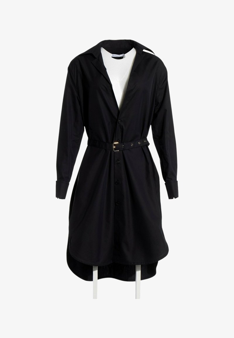 Robe-chemise noire à manches longues ceinturée avec col et boutons sur un top blanc, exposée sur un mannequin blanc.
