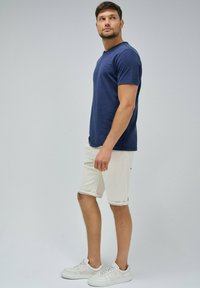 Granatowa koszulka z krótkim rękawem w połączeniu z białymi szortami do kolan. Model nosi białe sneakersy. Prosty, casualowy design z minimalnymi detalami.