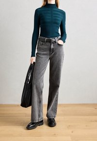 Pull turtleneck côtelé bleu canard avec des rayures horizontales, associé à un jean large taille haute gris et des chaussures à plateforme noires. Sac noir �à la main.