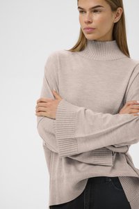 Ljus beige tröja med hög ribbad krage, vida ärmar och ribbad nederdel. Mjuk textur, lagerdesign och avslappnad passform.