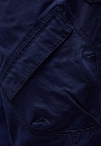 Marineblå stofshorts med en struktureret overflade, der har et markant vinkelformet lomme-design og et lille logoemblem.