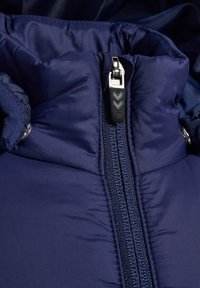 Marinblå vadderad jacka med en dragkedja med svart grepphandtag, slät textur och sydda detaljer runt kragen.