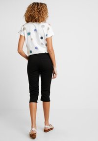 Camiseta blanca con patrones de puntos coloridos, combinada con pantalones cortos negros. Presenta un corte holgado y mangas cortas, demostrando un estilo informal.