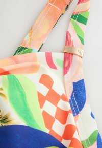 Pestrobarevná bikiny horní část s jasnými květinovými a geometrickými vzory, vyrobená z hladkého materiálu. Obsahuje zlatou kovovou sponu na růžovém popruhu.