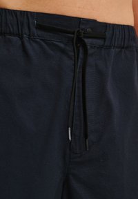 Shorts bleu marine en tissu doux, dotés d'une taille élastique avec cordon de serrage et d'une poche latérale. Texture lisse et design simple.
