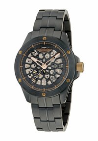 Černé metalové hodinky se skeleton ciferníkem, zlatými akcenty a vzorovaným čelem. Disponují robustním designem náramku s články a výraznou korunou.