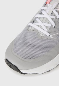 Nærbilde av grå og hvit joggesko med mesh-overdel, hvite snørebånd, og "Ultra Flow 2"-etikett på tungen.