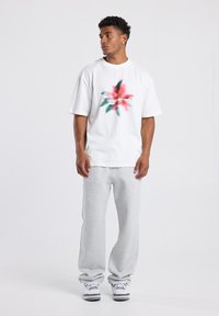 Camiseta de algodón blanca con un gráfico floral colorido y texto, combinada con pantalones de chándal gris claro y zapatillas blancas.