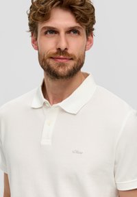 Weißes Poloshirt aus strukturiertem Stoff, mit klassischem Kragen, kurzen Ärmeln und kleinem gesticktem Logo auf der Brust.