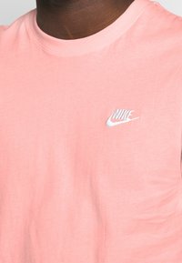 T-shirt in cotone rosa chiaro con colletto a girocollo e maniche corte. Presenta un piccolo logo Nike ricamato in bianco sul petto.