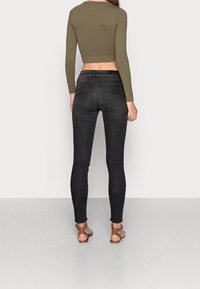 Jeans negros ajustados con una cintura de altura media, complementados con un top corto ajustado de color verde oliva. Sandalias con acentos en bronce completan el look.