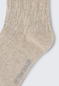 Beige kötött zoknik texturált mintával, megerősített lábujjjal és sarkal. A "TOM TAILOR" márka felirata szürkével van nyomtatva a felső részen.