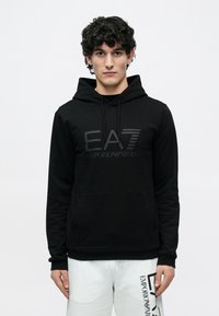 Svart hettegenser med kengurulomme, med et ton-i-ton EA7-logo og teksten "EMPORIO ARMANI". Mykt, glatt stoff med justerbar hette.