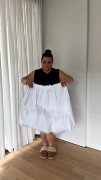 White, mid-length skirt made of lightweight material, featuring gathered fabric at the waist. A person holds the skirt, wearing brown slippers.