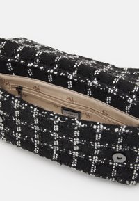 Pochette en tweed noir et blanc avec un motif texturé, équipée d'une poche zippée à l'intérieur et d'une étiquette de logo. Accents en métal argenté au niveau de la fermeture.