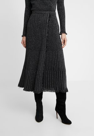 Femme portant une jupe midi en maille côtelée noire avec des bords à franges, associée à des bottes hautes à talons en daim noir jusqu'aux genoux.