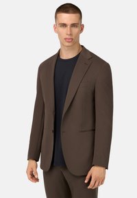 Ruskea puku takki, jossa on yksi nappi, kaksi etutaskua, viistetyt läp�ät, käytetty tummansinisen T-paidan päällä. Liukas pinta, räätälöity istuvuus.