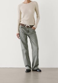 Beige geribbelde trui met lange mouwen, gecombineerd met lichtgrijze jeans met rechte pijpen en een bruine riem met een ronde zilveren gesp. Zwarte ballerina's.