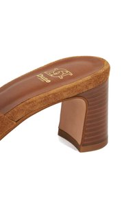 Glissière à talon bloc en suede marron avec une semelle intérieure lisse marron et un accent en bois strié sur le talon. Logo doré sur le pied.
