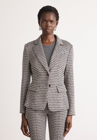 Gray and black patterned blazer with a fitted design, notch lapels, two front pockets, and two buttons. Paired with a gray top beneath.