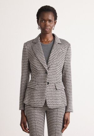 Grijze en zwarte geblokte blazer met een getailleerd ontwerp, notch revers, twee voorkjassen, en twee knopen. Gepaard met een grijze top eronder.