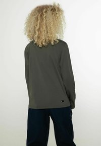 Grünes Langarmshirt aus glattem, dehnbarem Stoff, mit lockerer Passform und dezentem Logo-Tag an der unteren Seite.