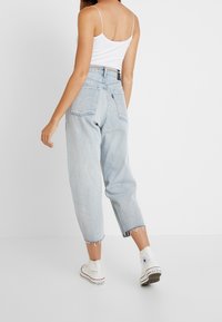 Jeans de tiro alto en un tono azul claro, con un corte relajado y dobladillos deshilachados; combinados con zapatillas de lona blancas. Presenta dos bolsillos traseros.