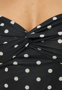 Tissu noir à pois blancs noué au centre, dévoilant une petite portion de peau au-dessus du vêtement.