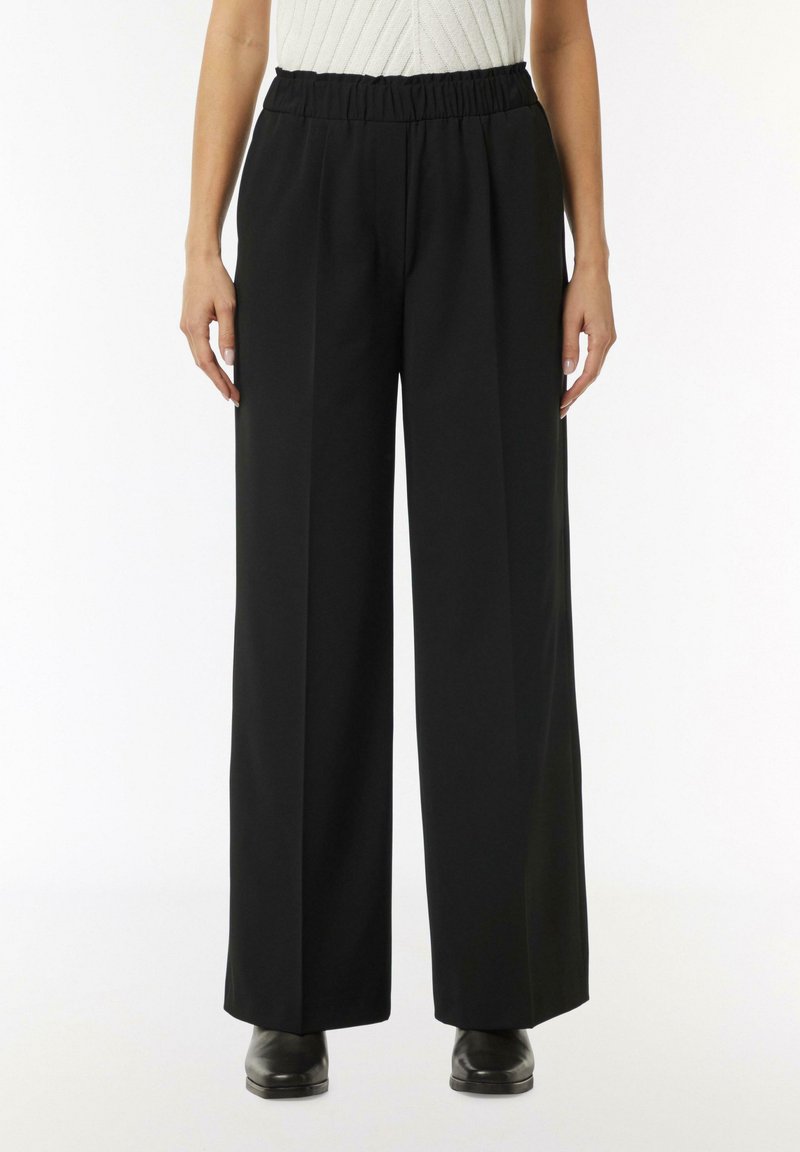 Black wide-leg trousers with an elastic waistband, featuring a smooth texture and side pockets. Material appears lightweight and flowy.
