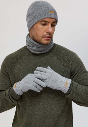Beanie grigio a maglia, guanti coordinati e una sciarpa grigia chiara, abbinati a un maglione verde scuro. Include un'etichetta piccola sugli accessori.