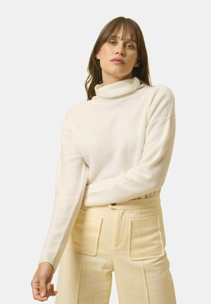 Cremefarvet turtleneck sweater med struktureret strik, lange ærmer og en afslappet pasform, parret med højtaljede beige bukser med lommer.