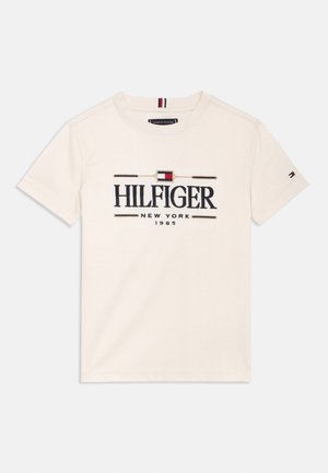 Krém színű rövid ujjú póló "HILFIGER NEW YORK 1985" felirattal, valamint egy kis piros, fehér és kék logóval a mellkason és az ujjon.