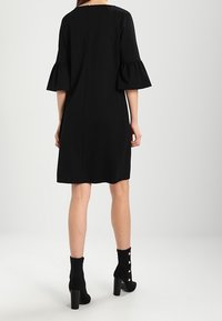 Svart klänning med utsvängda korta ärmar, knä-lång, texturerad tyg och en dold dragkedja bak. Bärs med svarta ankelstövlar med guldknappar.