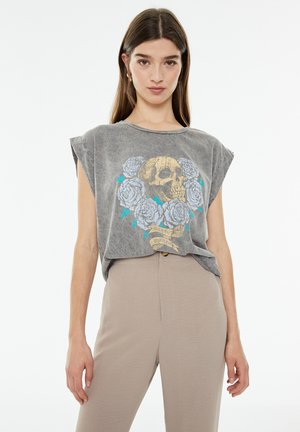 Camiseta sin mangas gris con un gráfico de calavera rodeado de rosas azules. Tela suave con un corte relajado y cuello redondo.